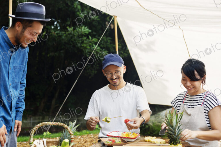 Two Japanese men and woman gathered around a table under a canopy, preparing fresh fruit.