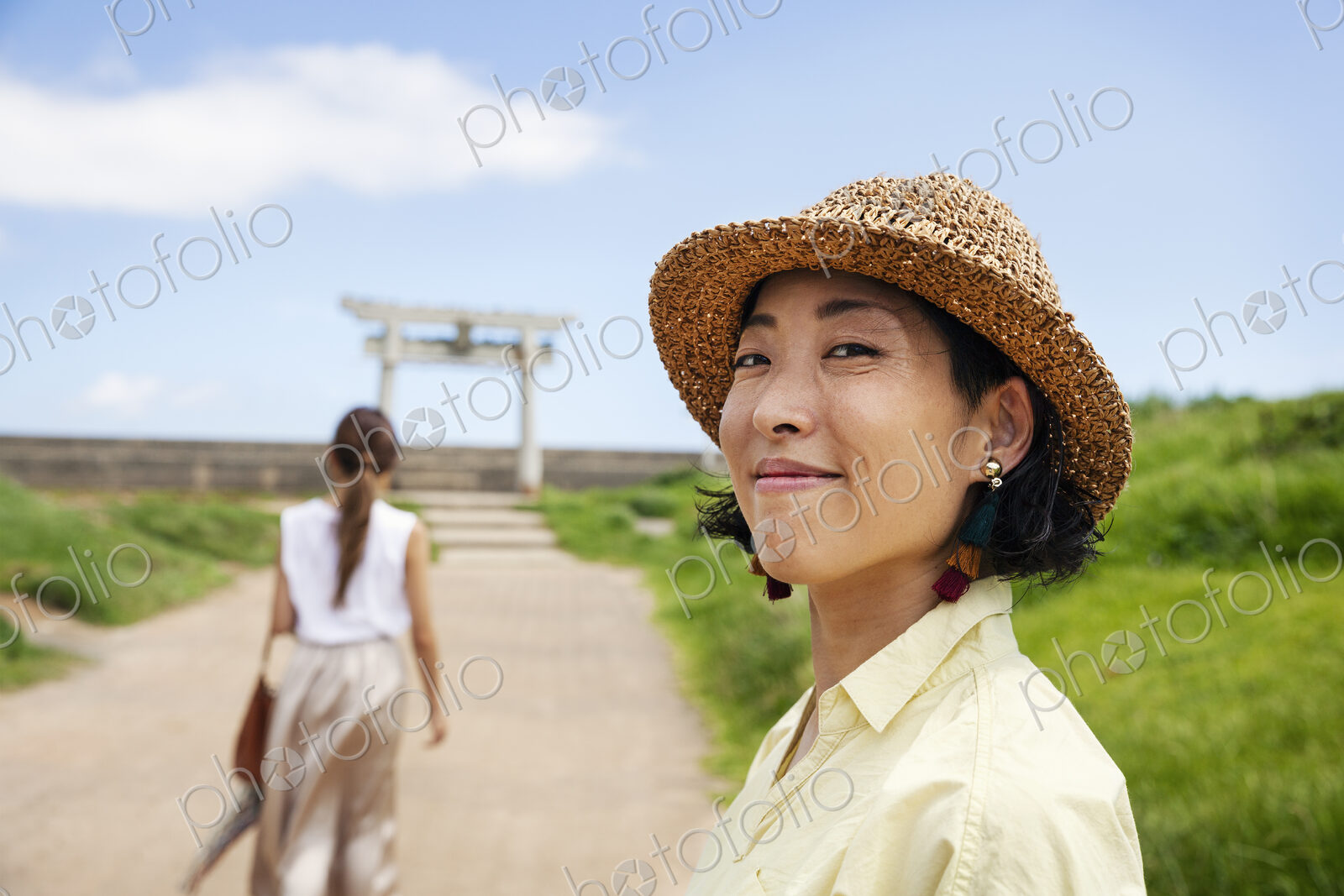 Two Japanese woman wearing hats standing on a path, Shinto shrine in the background.
