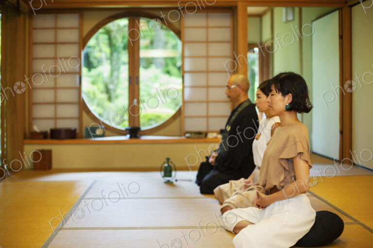 Two Japanese women and Buddhist priest kneeling in Buddhist temple, praying.