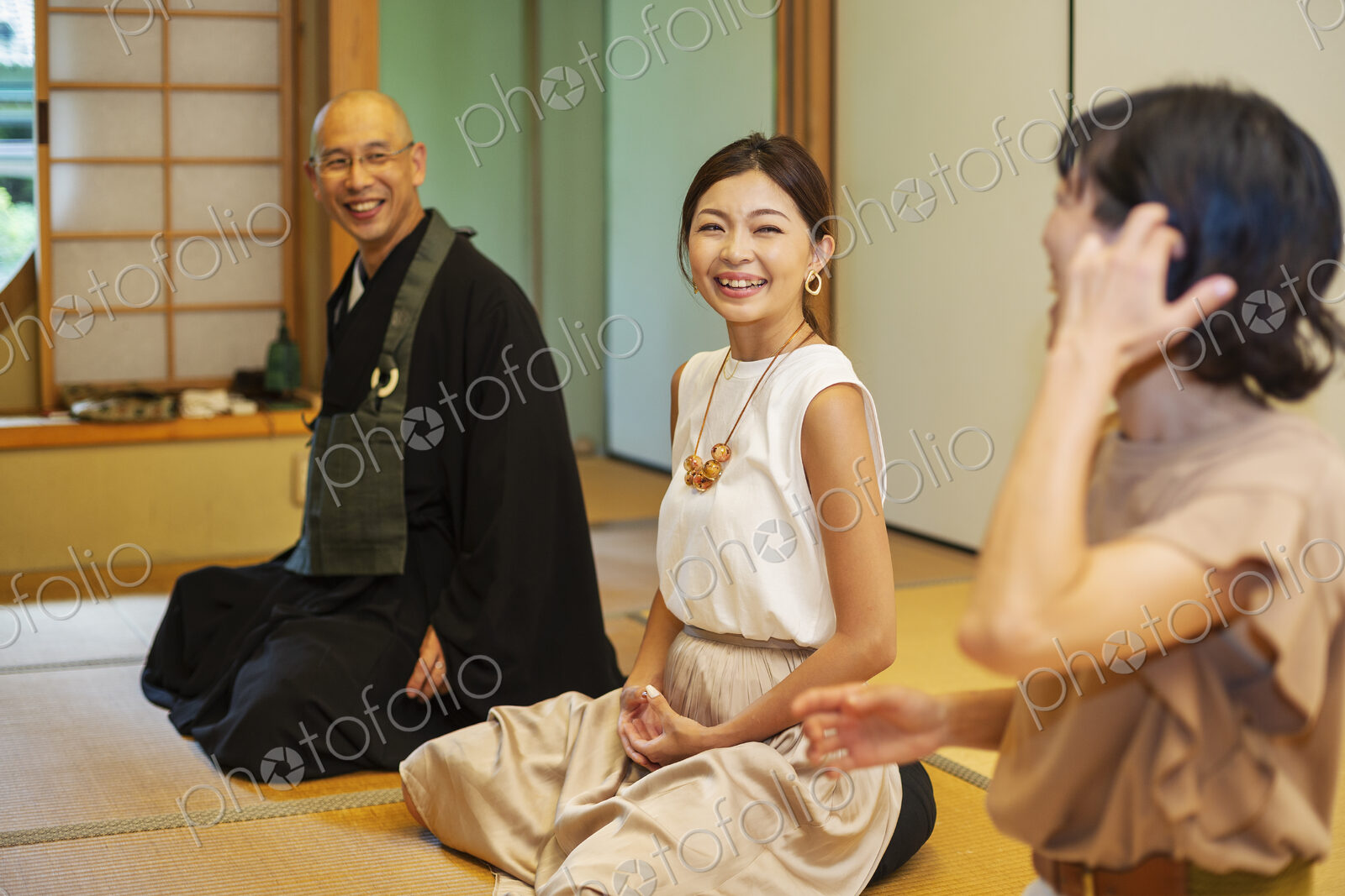 Two Japanese women and Buddhist priest kneeling in Buddhist temple, talking.