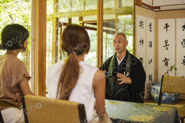Two Japanese women and Buddhist priest kneeling in Buddhist temple, talking.