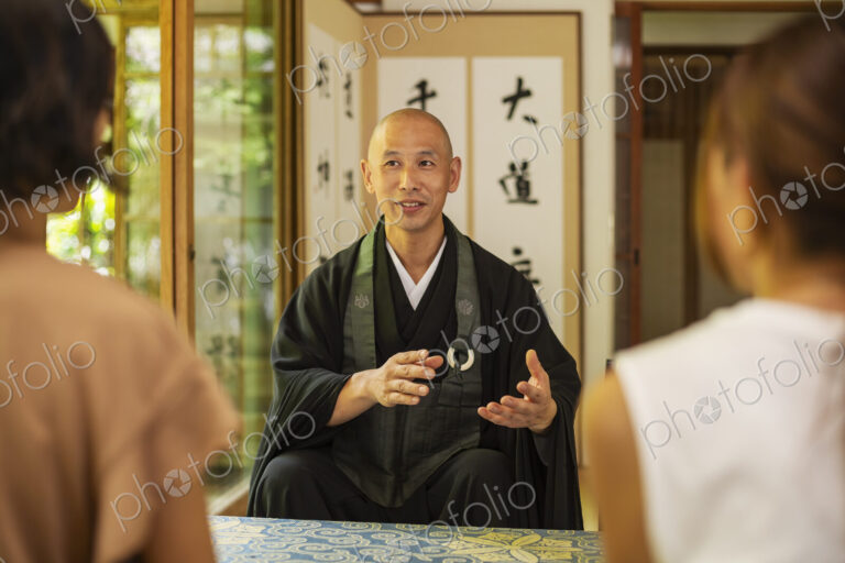 Two Japanese women and Buddhist priest kneeling in Buddhist temple, talking.