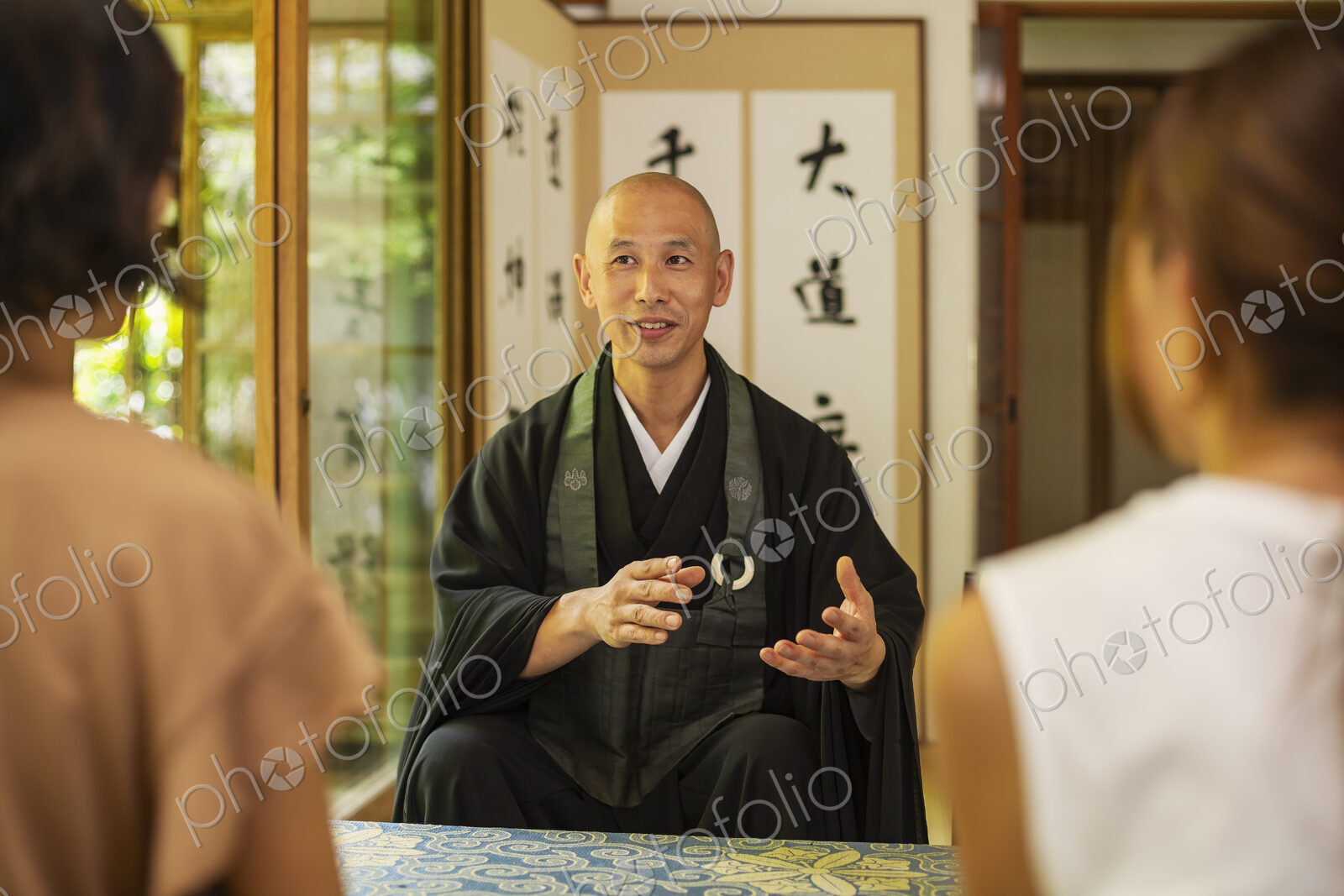 Two Japanese women and Buddhist priest kneeling in Buddhist temple, talking.