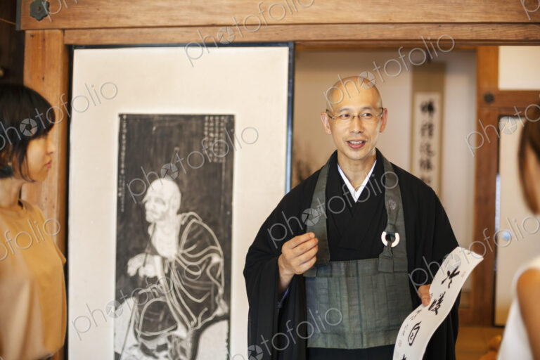 Two Japanese women and Buddhist priest standing in Buddhist temple, talking.