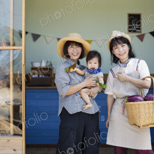 Two Japanese women and boy standing outside a farm shop, smiling at camera.