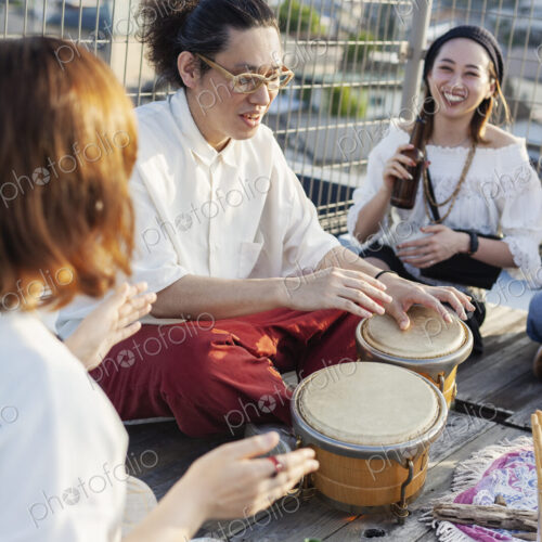 Two Japanese women and man sitting on a rooftop in an urban setting, playing drums. Two Japanese women and man sitting on a rooftop in an urban setting, playing drums.