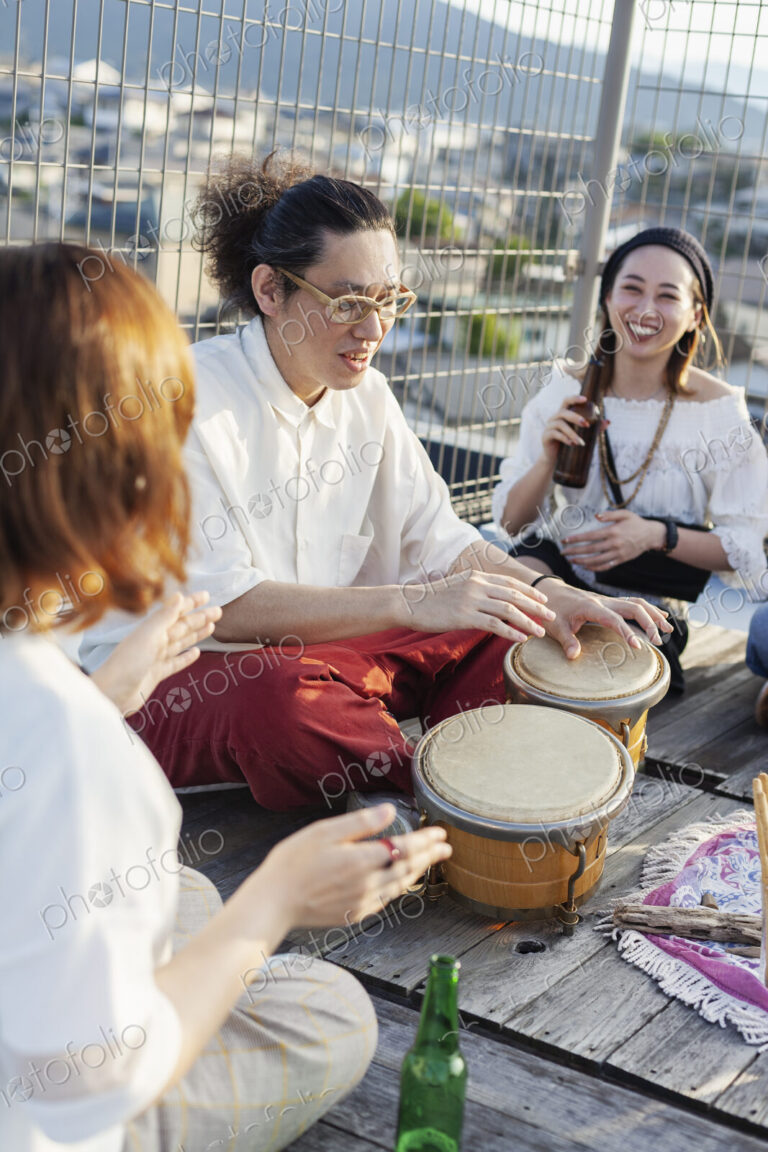 Two Japanese women and man sitting on a rooftop in an urban setting, playing drums.