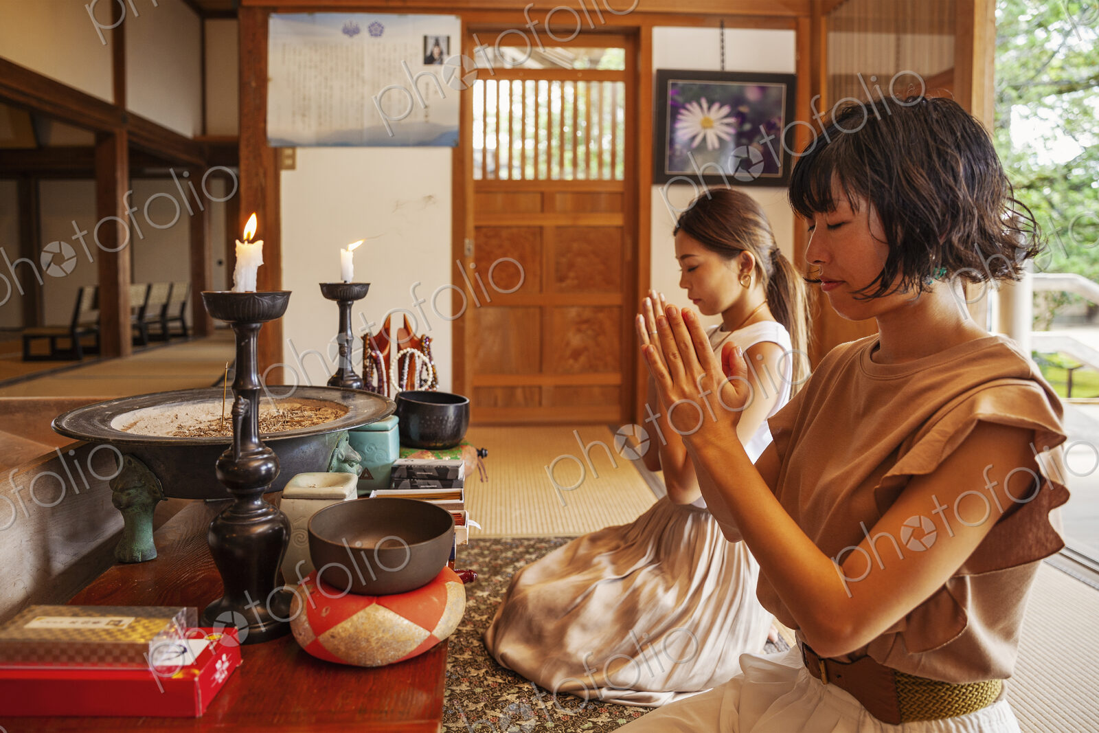 Two Japanese women kneeling in Buddhist temple, praying.