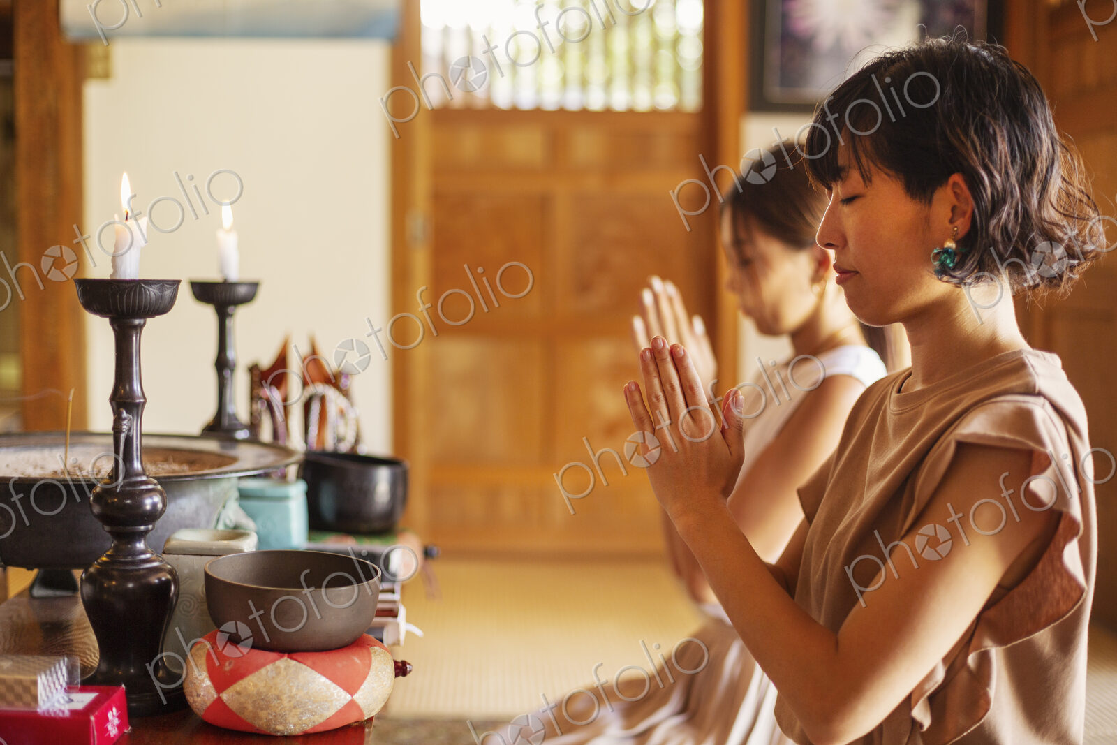 Two Japanese women kneeling in Buddhist temple, praying.