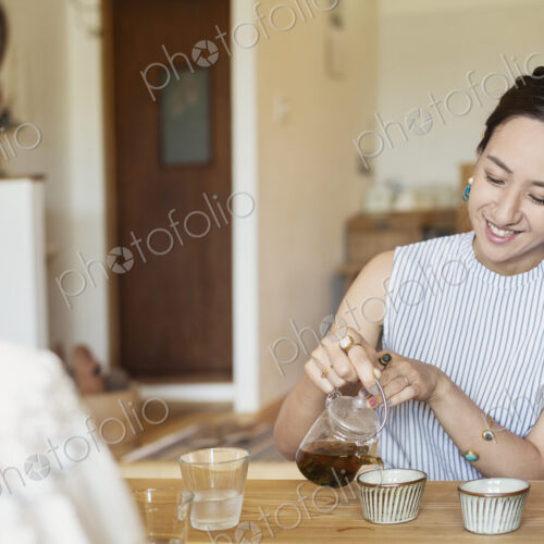 Two Japanese women sitting at a table in a vegetarian cafe, pouring tea. Two Japanese women sitting at a table in a vegetarian cafe, pouring tea.