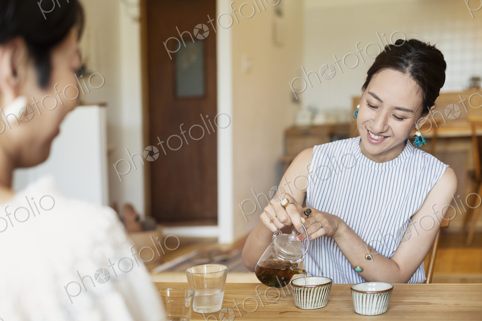Two Japanese women sitting at a table in a vegetarian cafe, pouring tea.
