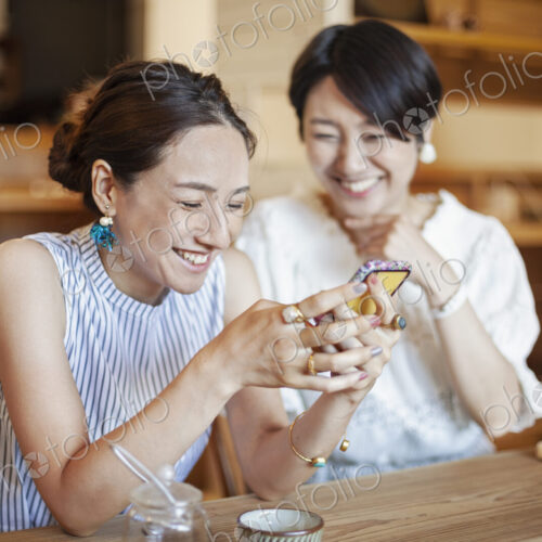 Two Japanese women sitting at a table in a vegetarian cafe, using mobile phone. Two Japanese women sitting at a table in a vegetarian cafe, using mobile phone.