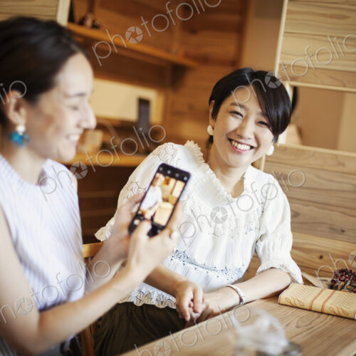 Two Japanese women sitting at a table in a vegetarian cafe, using mobile phone. Two Japanese women sitting at a table in a vegetarian cafe, using mobile phone.