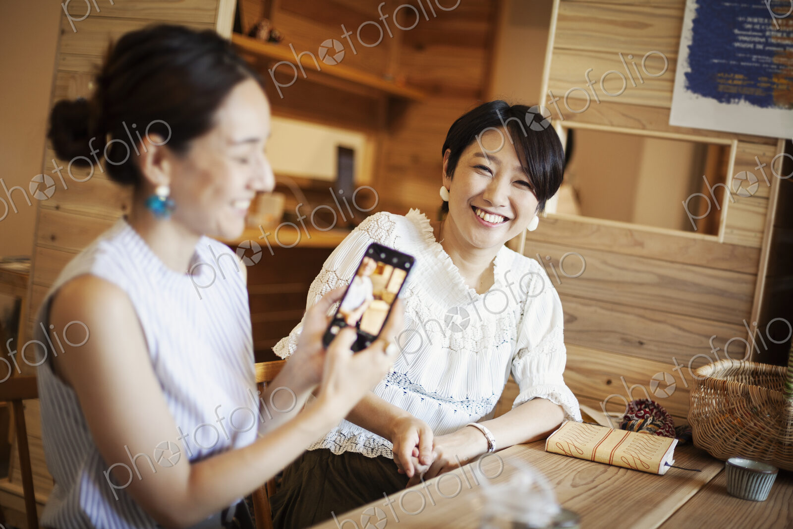 Two Japanese women sitting at a table in a vegetarian cafe, using mobile phone.