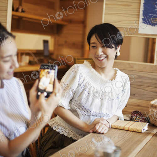 Two Japanese women sitting at a table in a vegetarian cafe, using mobile phone. Two Japanese women sitting at a table in a vegetarian cafe, using mobile phone.