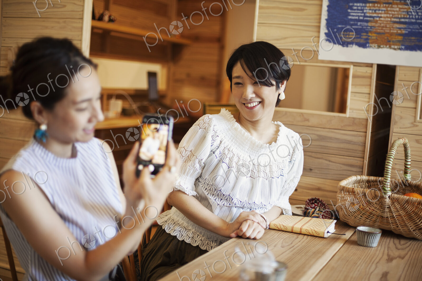 Two Japanese women sitting at a table in a vegetarian cafe, using mobile phone.