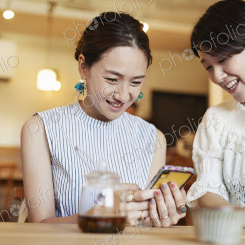 Two Japanese women sitting at a table in a vegetarian cafe, using mobile phone. Two Japanese women sitting at a table in a vegetarian cafe, using mobile phone.