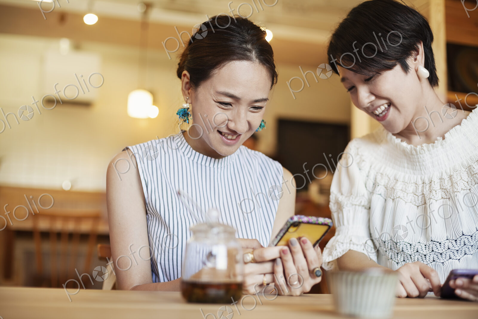 Two Japanese women sitting at a table in a vegetarian cafe, using mobile phone.