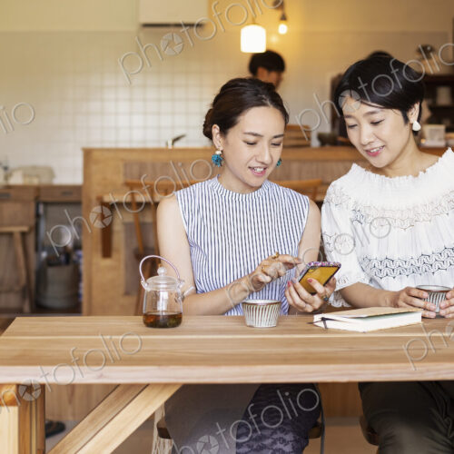 Two Japanese women sitting at a table in a vegetarian cafe, using mobile phone. Two Japanese women sitting at a table in a vegetarian cafe, using mobile phone.