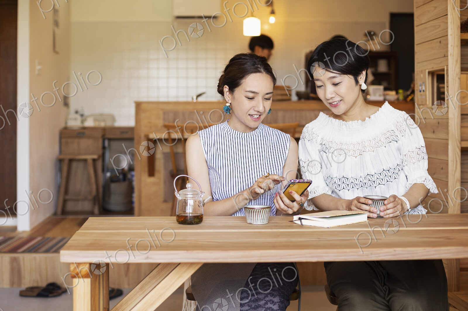 Two Japanese women sitting at a table in a vegetarian cafe, using mobile phone.