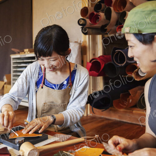 Two Japanese women sitting at a table, working in a leather shop.
