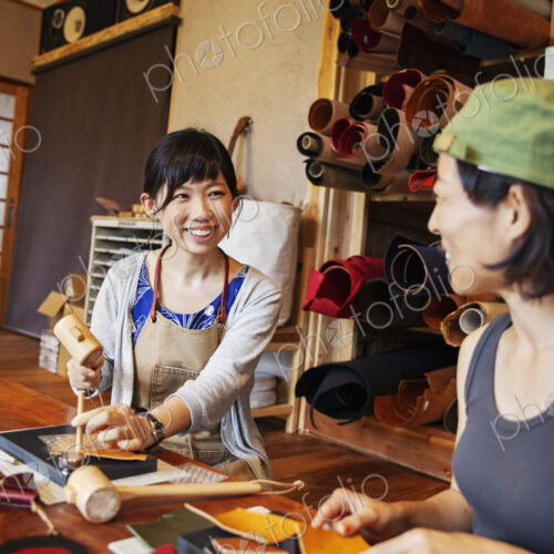 Two Japanese women sitting at a table, working in a leather shop.
