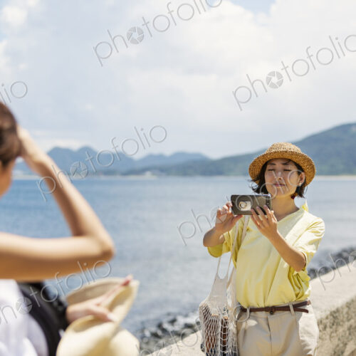 Two Japanese women standing by the ocean, taking picture with mobile phone. Two Japanese women standing by the ocean, taking picture with mobile phone.