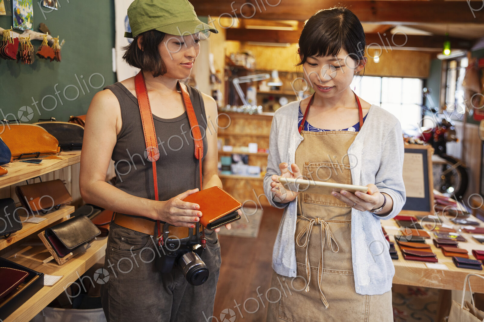Two Japanese women standing in a leather shop, holding leather purse and digital tablet.