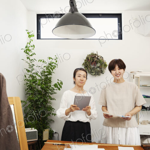 Two Japanese women standing in a small fashion boutique, holding digital tablet,… Two Japanese women standing in a small fashion boutique, holding digital tablet,…