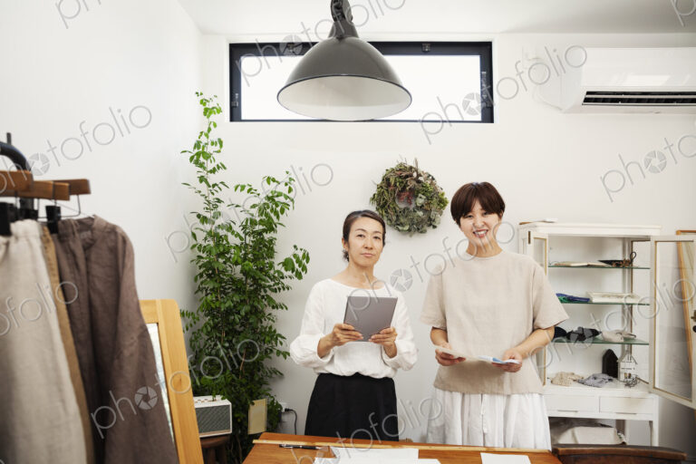 Two Japanese women standing in a small fashion boutique, holding digital tablet,…