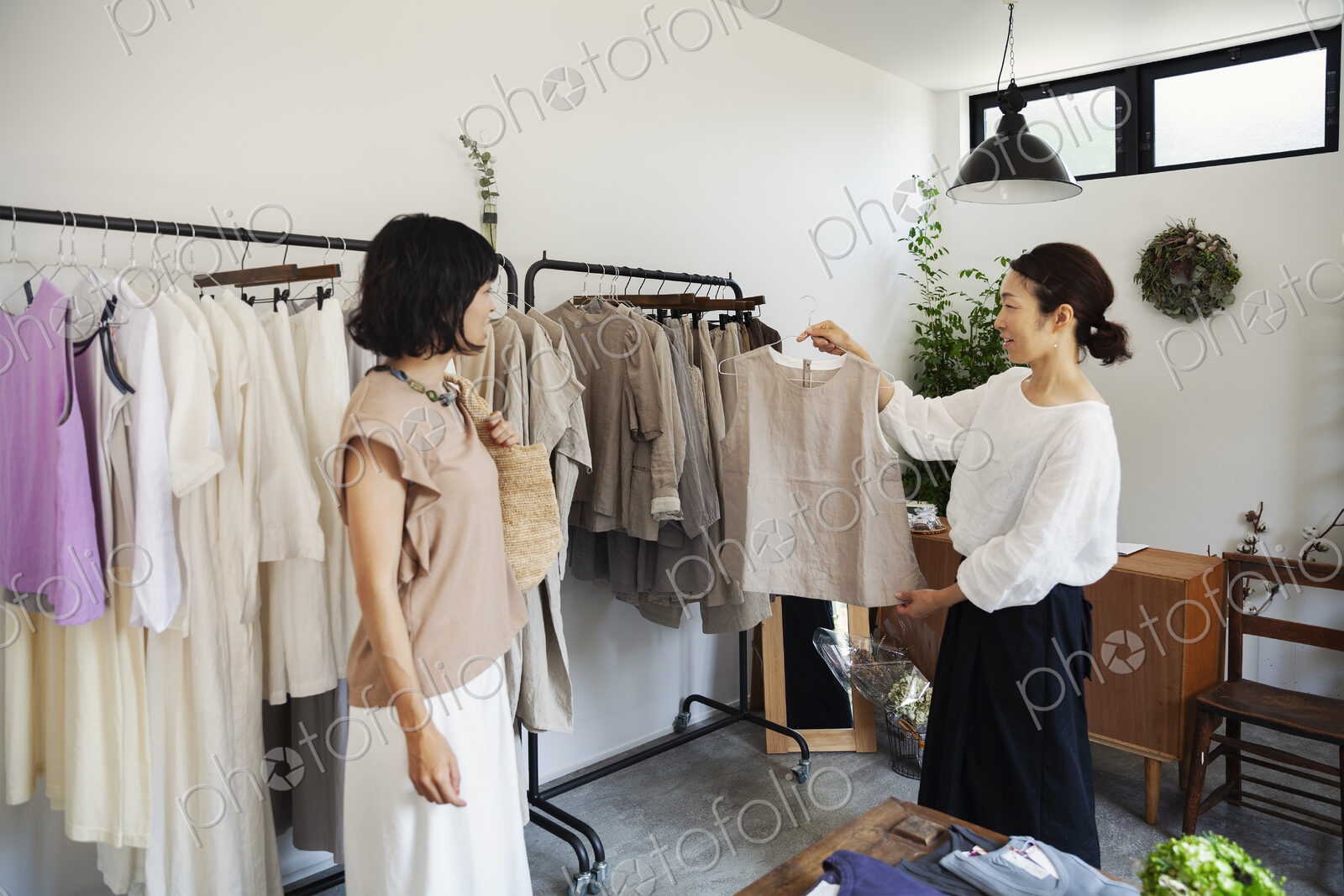 Two Japanese women standing in a small fashion boutique, looking at tops.