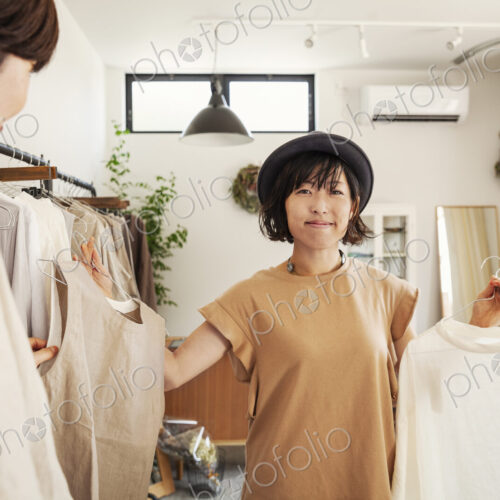 Two Japanese women standing in a small fashion boutique, looking at tops.