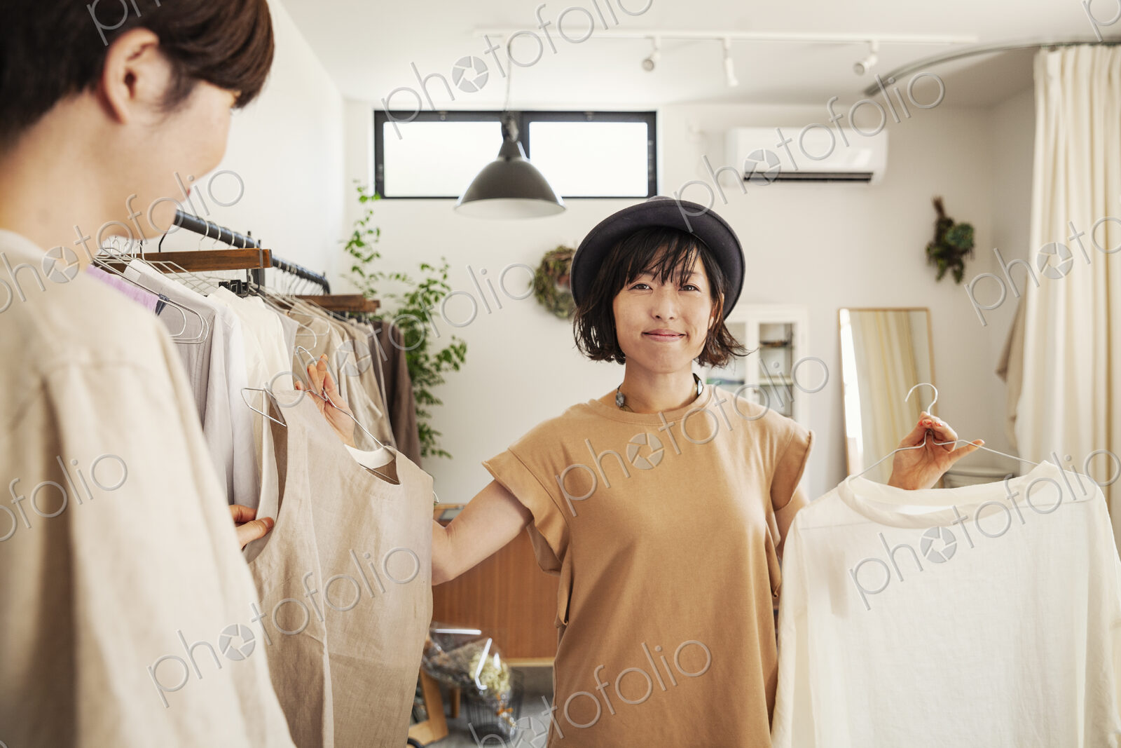 Two Japanese women standing in a small fashion boutique, looking at tops.