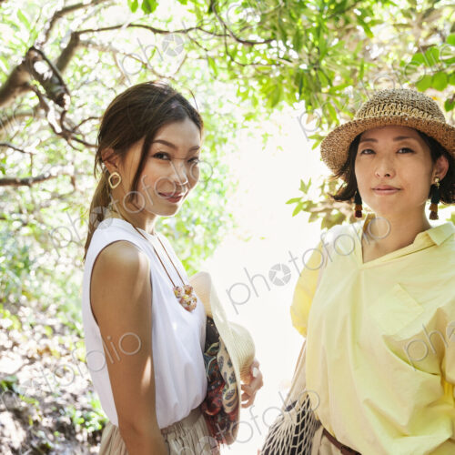 Two Japanese women wearing hats hiking in a forest. Two Japanese women wearing hats hiking in a forest.
