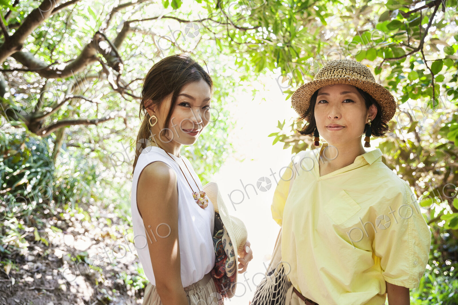 Two Japanese women wearing hats hiking in a forest.
