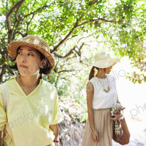 Two Japanese women wearing hats hiking in a forest.