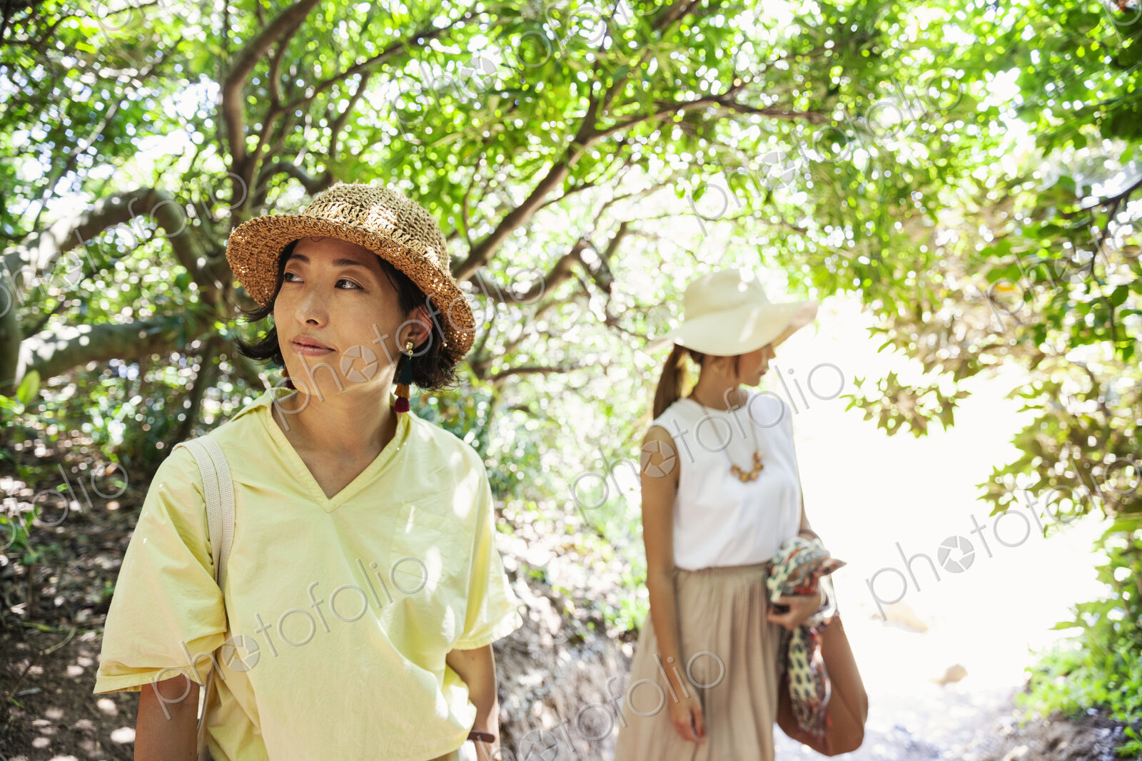 Two Japanese women wearing hats hiking in a forest.