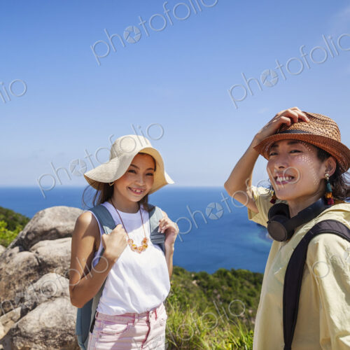 Two Japanese women wearing hats standing on a cliff, ocean in the background. Two Japanese women wearing hats standing on a cliff, ocean in the background.