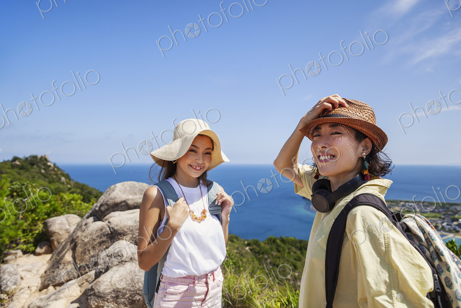 Two Japanese women wearing hats standing on a cliff, ocean in the background.