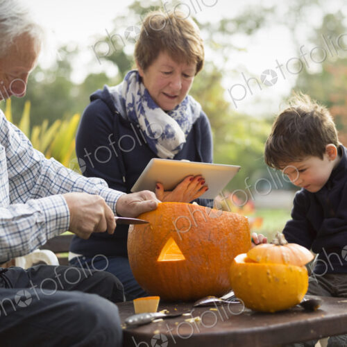 Two adults and a small child with large pumpkins, creating pumpkin lanterns for Halloween.