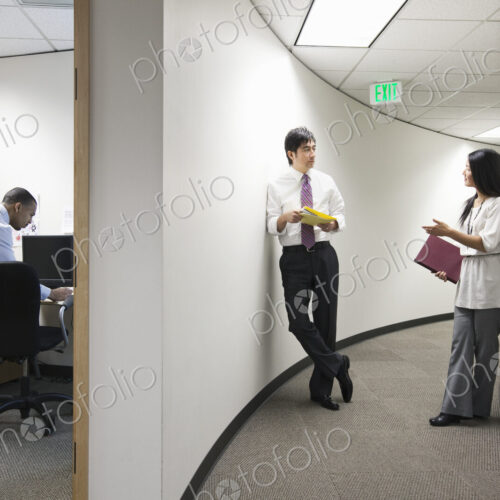 Two asian businesspeople talking in a hallway near a black businessman working alone… Two asian businesspeople talking in a hallway near a black businessman working alone…