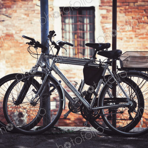 Two bicycles resting against a post in Venice outside a building.