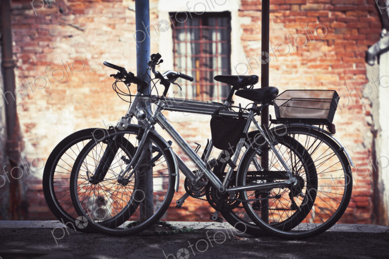 Two bicycles resting against a post in Venice outside a building.