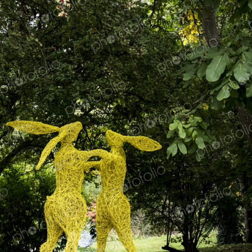 Two boxing hares on hind legs, a tall garden sculpture painted in yellow.