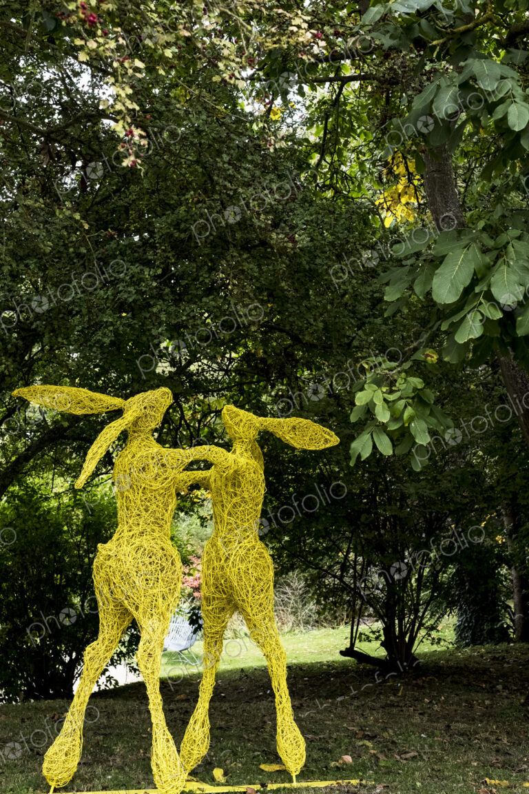 Two boxing hares on hind legs, a tall garden sculpture painted in yellow.
