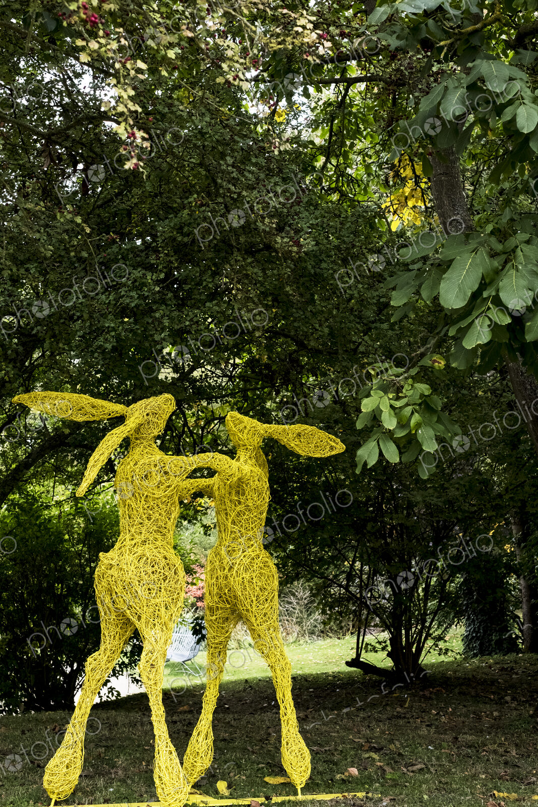 Two boxing hares on hind legs, a tall garden sculpture painted in yellow.