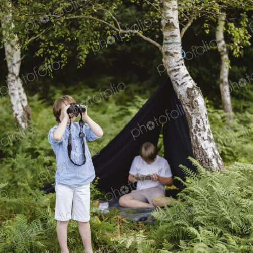 Two boys camping in New Forest. One sitting under a black canvas shelter. One boy… Two boys camping in New Forest. One sitting under a black canvas shelter. One boy…