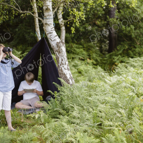 Two boys camping in New Forest. One sitting under a black canvas shelter. One boy… Two boys camping in New Forest. One sitting under a black canvas shelter. One boy…