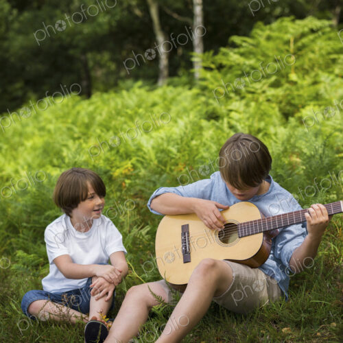 Two boys camping in New Forest. Sitting on the grass, one playing a guitar. Two boys camping in New Forest. Sitting on the grass, one playing a guitar.