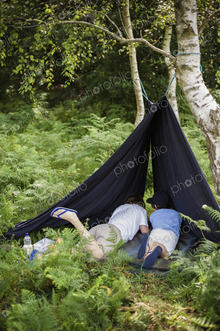 Two boys camping in the New Forest lying under a canvas shelter.